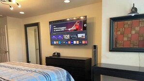 Une chambre à coucher comprenant un lit, une commode, un téléviseur fixé au mur et un tableau encadré au-dessus de la commode.