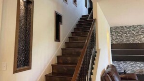 Un escalier avec des marches en bois foncé et une rampe en métal, menant à un palier dont le mur est orné d’un motif.
