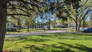 A residential street with houses, trees, and a grassy area.