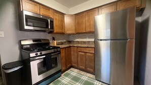Una cocina con armarios de madera, un refrigerador de acero inoxidable, un microondas y una estufa.