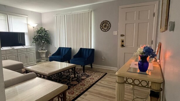 Una sala de estar con un sofá, dos sillones, una mesa de centro, un televisor, una planta en maceta, un plato decorativo y un jarrón con flores.