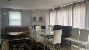 Una sala de estar moderna con una mesa de comedor de vidrio, sillas blancas, un sofá marrón y una alfombra floral negra.