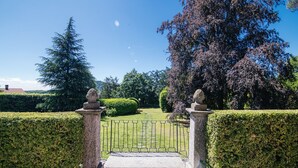 A formal garden with a paved pathway leading to a gated entrance.