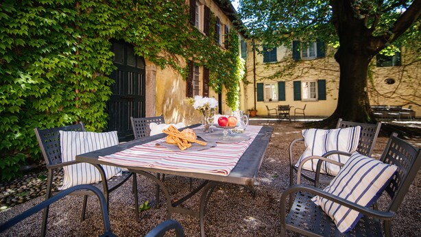 An outdoor patio with a table set for two, surrounded by metal chairs with striped cushions.