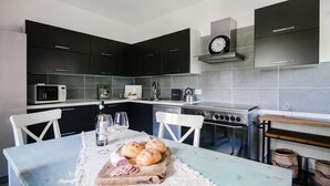 A modern kitchen with dark cabinets, a microwave, a stove, and a dining table with bread and cheese.