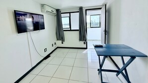 A room with a flat-screen TV mounted on the wall, a window with curtains, a door, and a blue table. - Céu Beach club (Rio de Janeiro)