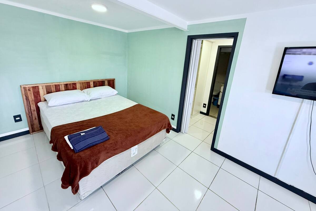 Habitación de hotel con cama, televisor y baño visible a través de una puerta abierta.