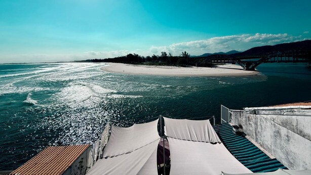 A beach view with a clear sky, a sandy shore, and a bridge in the distance. - Céu Beach club (Rio de Janeiro)