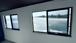 A room with two large windows overlooking a beach and ocean. - Céu Beach club (Rio de Janeiro)