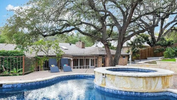 A swimming pool with a hot tub, surrounded by trees and a fenced patio area.