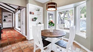 A dining area with a round wooden table, white chairs, and a hanging light fixture.