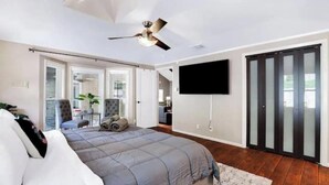 A bedroom with a bed, a ceiling fan, a TV, and a sliding door.