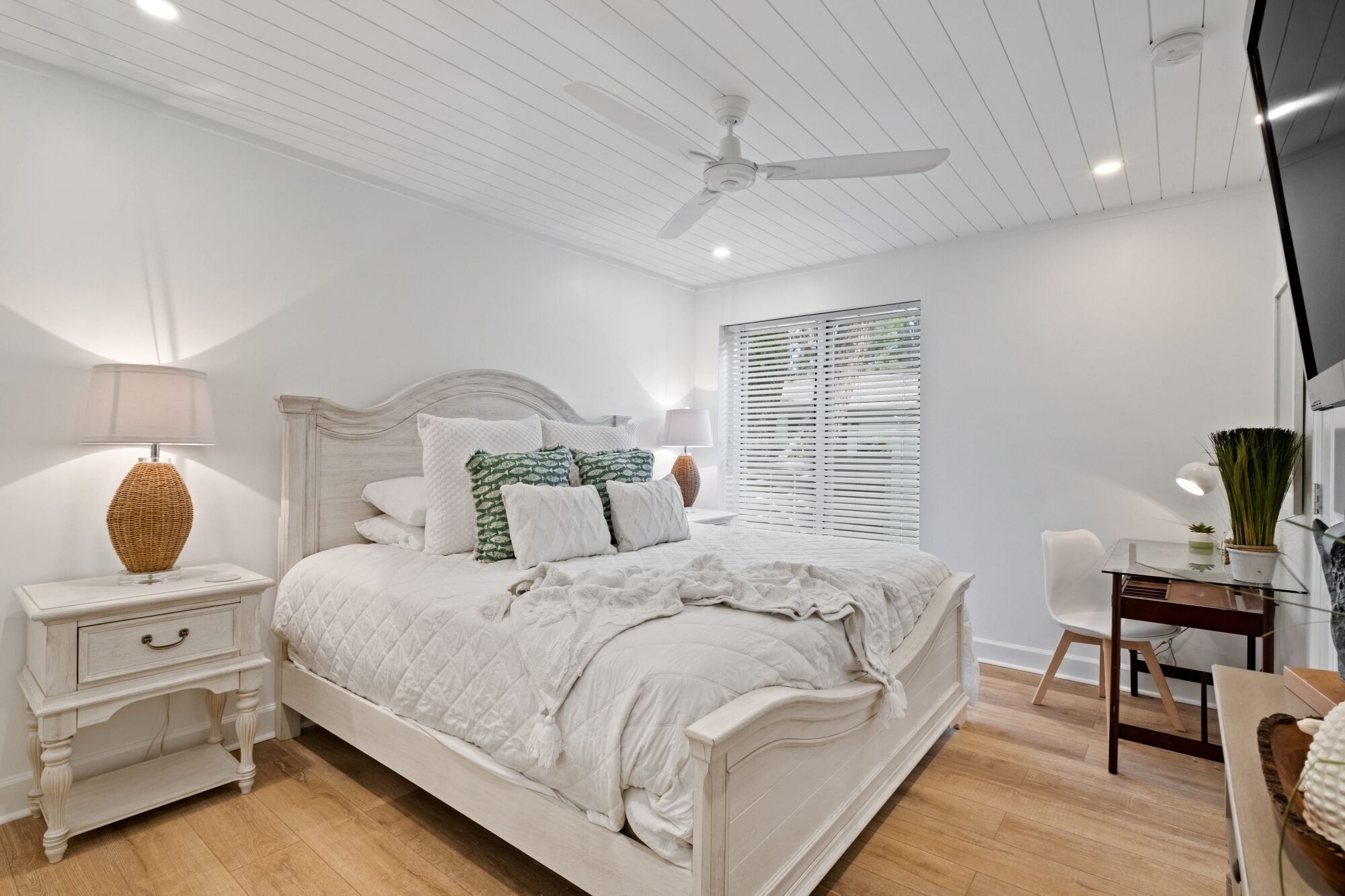 A bedroom with a bed, bedside tables, a desk, and a ceiling fan.