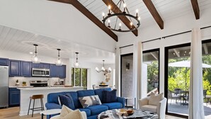 A spacious living area with a blue sofa, a leather ottoman, and a dining table. A kitchen with blue cabinets and a large island is visible in the background. - 1590 Lagoon Villas at The Sea Pines Resort (Hilton Head Island)