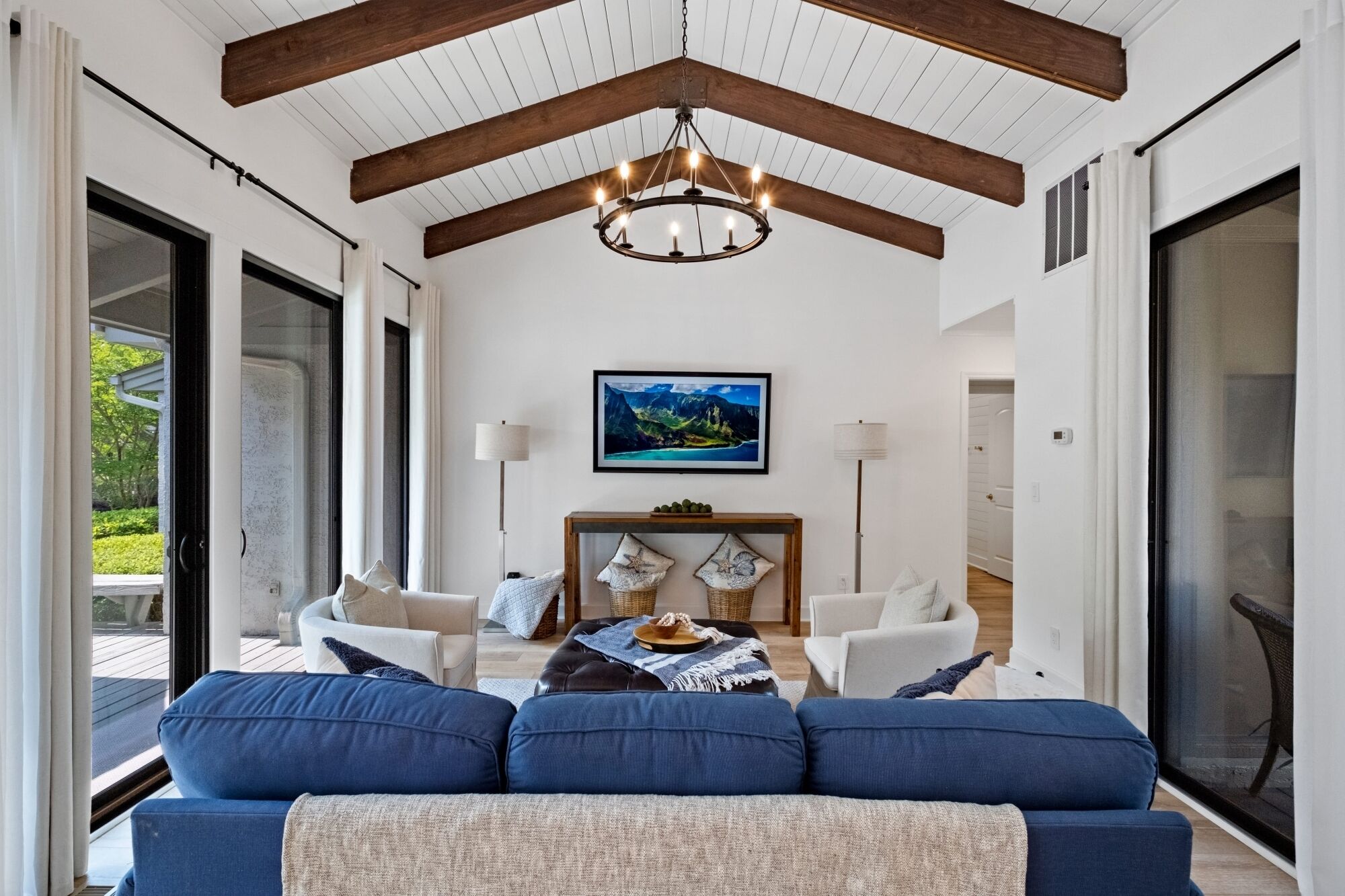 A spacious living room with a high ceiling, a chandelier, a large painting, and a view of the outdoors.