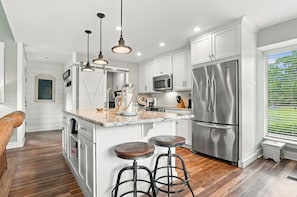 A modern kitchen with white cabinetry, stainless steel appliances, and a central island with stools.