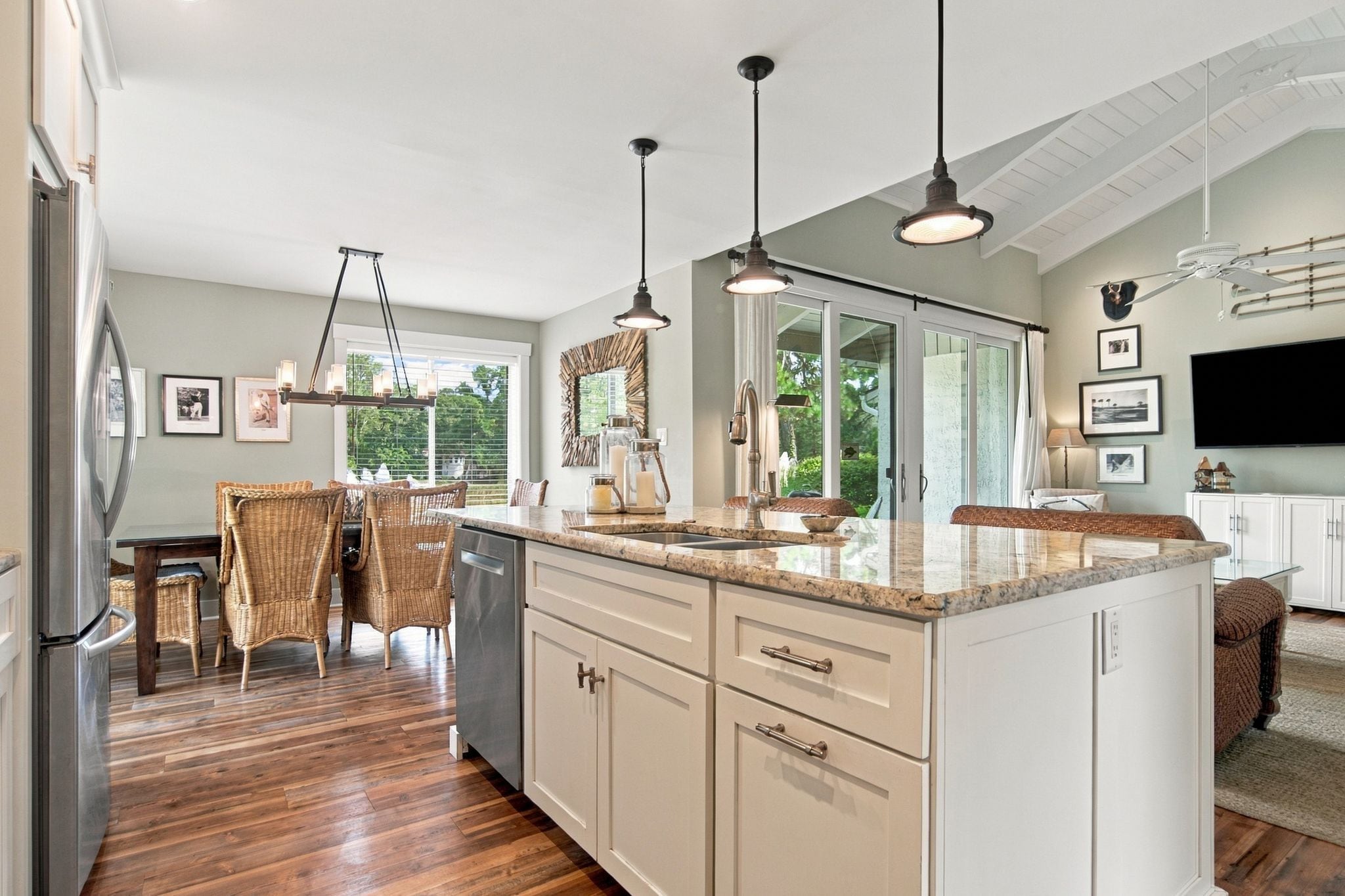 A modern kitchen with a large island, pendant lighting, and a dining area with wicker furniture.