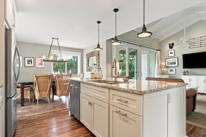 A modern kitchen with a large island, pendant lighting, and a dining area with wicker furniture. - 1596 Lagoon Villas at The Sea Pines Resort (Hilton Head Island)