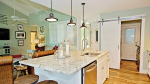 A kitchen with a central island, bar stools, a dishwasher, and a sliding door leading to another room. - 1596 Lagoon Villas at The Sea Pines Resort (Hilton Head Island)