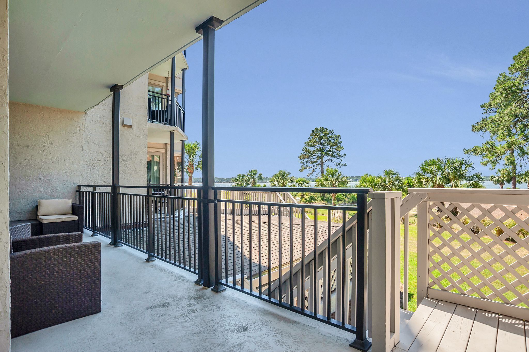 A balcony with wicker furniture and a view of a landscaped area with trees and a building in the background.