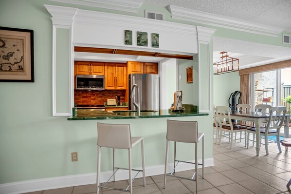 A kitchen with white cabinetry, a stainless steel refrigerator, and a glass island with two bar stools. - 1722 Bluff Villas at The Sea Pines Resort (Hilton Head Island)