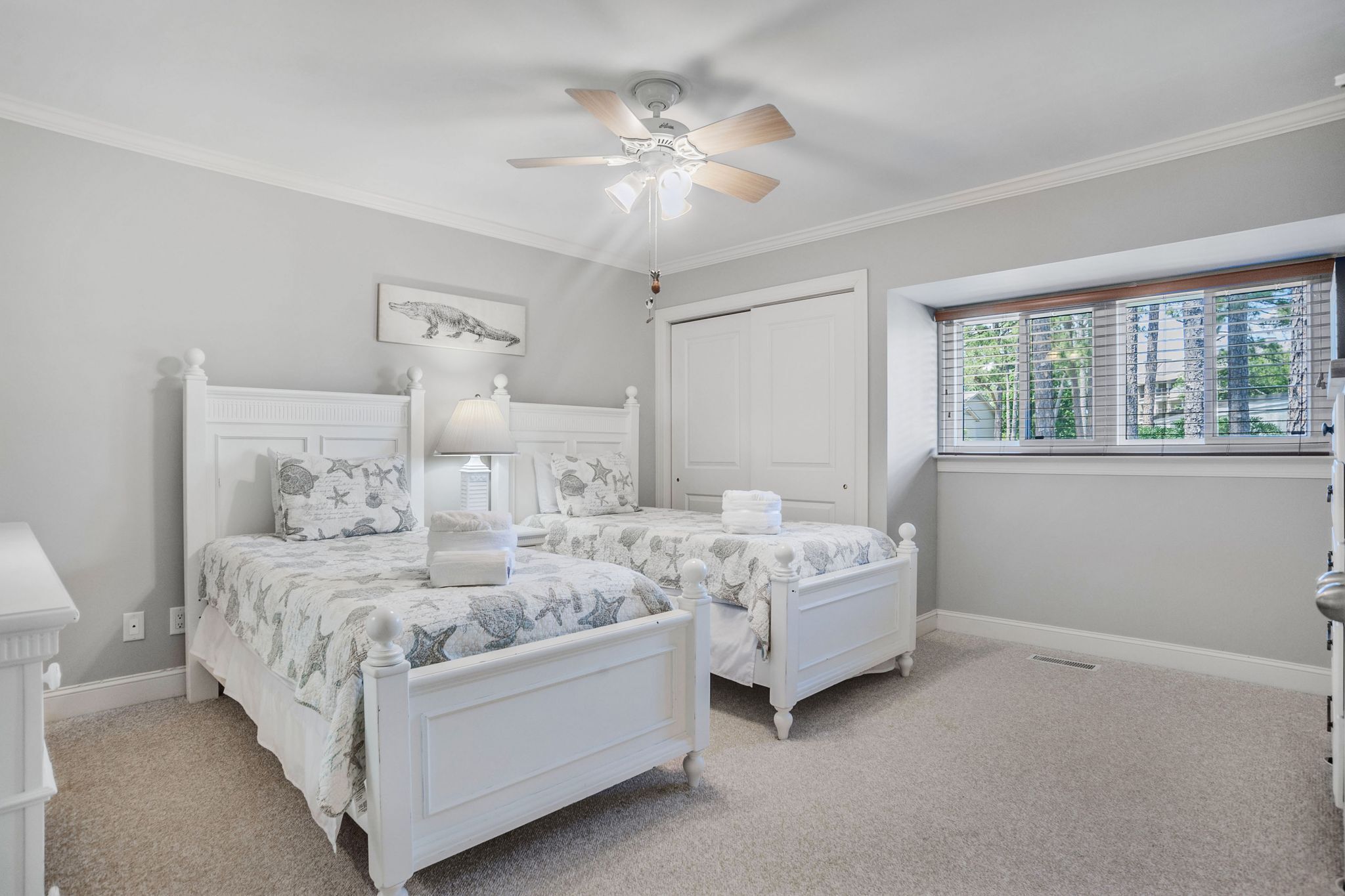 A bedroom with two white beds, a ceiling fan, a window with blinds, and a door.