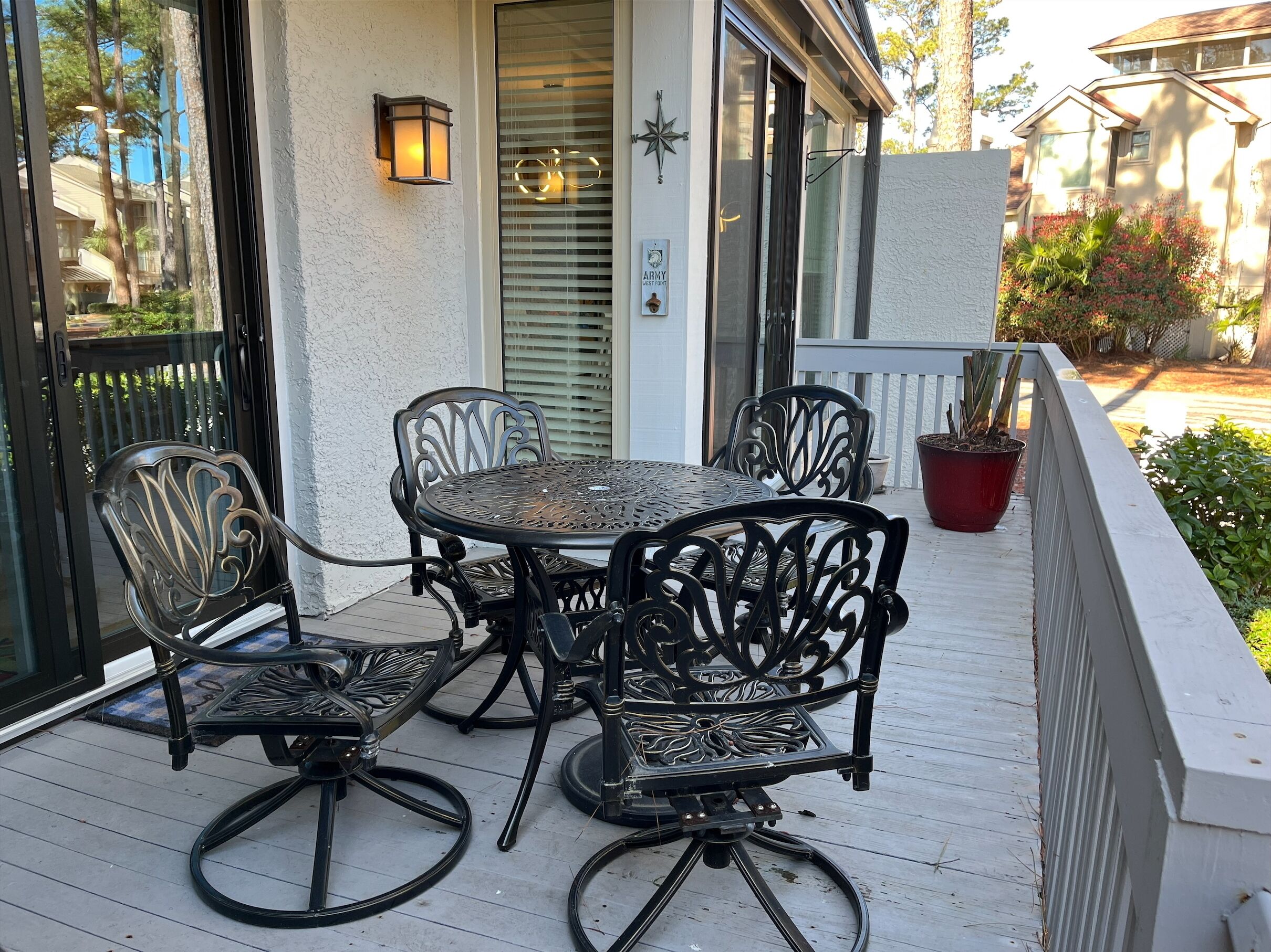 A patio with a round table and four chairs, a potted plant, and a wall-mounted light fixture.