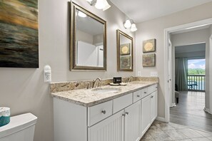 Un baño con lavamanos doble, tocador y un espejo grande. Hay luces empotradas en la pared y obras de arte sobre el espejo.