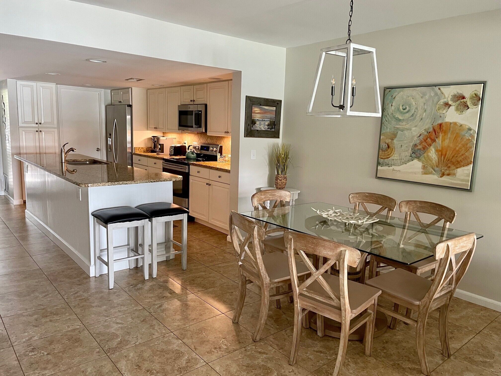 Una cocina moderna con armarios blancos, electrodomésticos de acero inoxidable y una mesa de comedor de vidrio con sillas de madera.