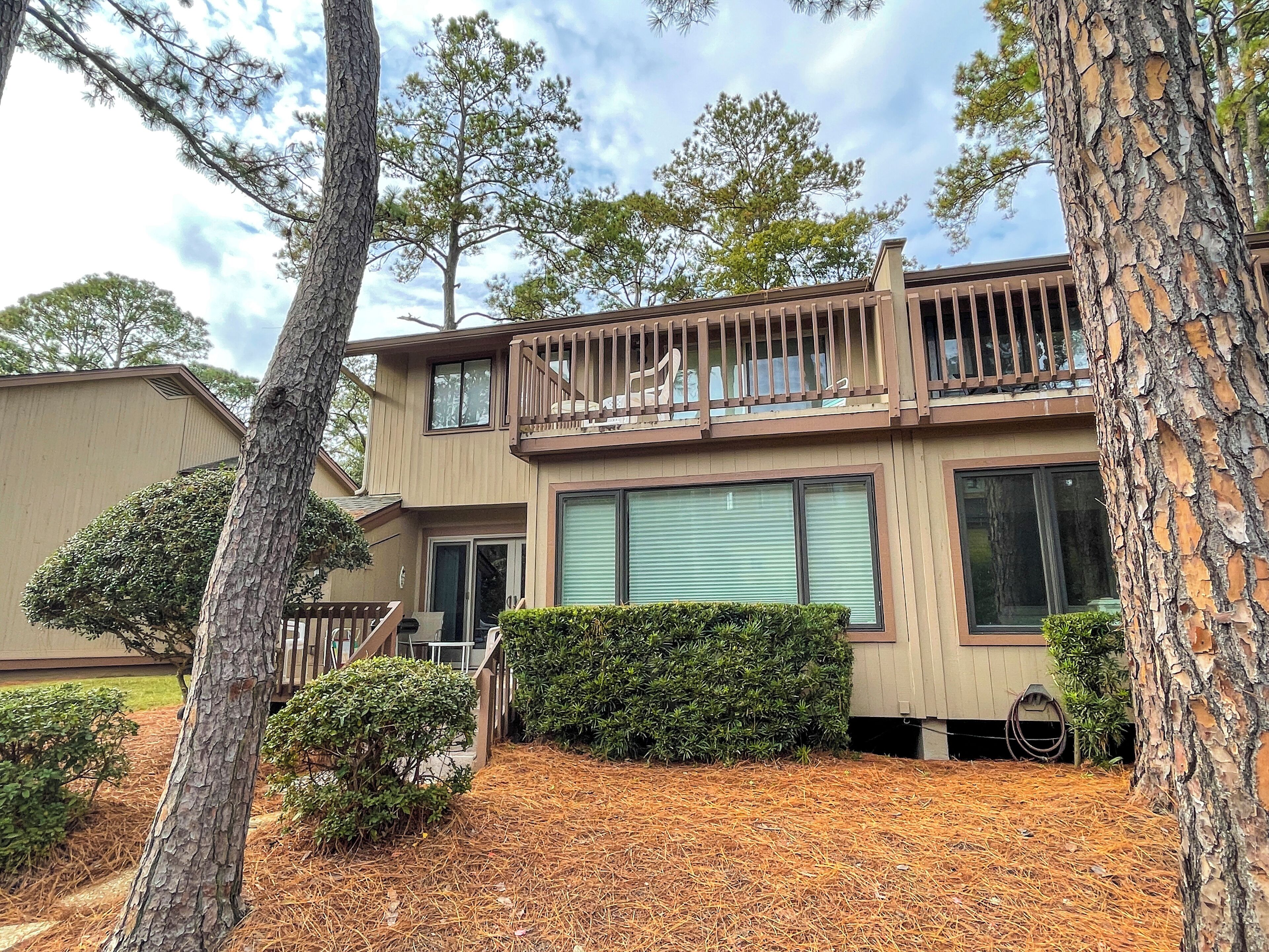 A two-story building with a balcony, surrounded by pine trees and a well-maintained lawn.
