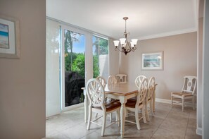 A dining area with a table and chairs, large windows with a view of greenery, and a chandelier. - 1270 Harbour Town Club at The Sea Pines Resort (Hilton Head Island)