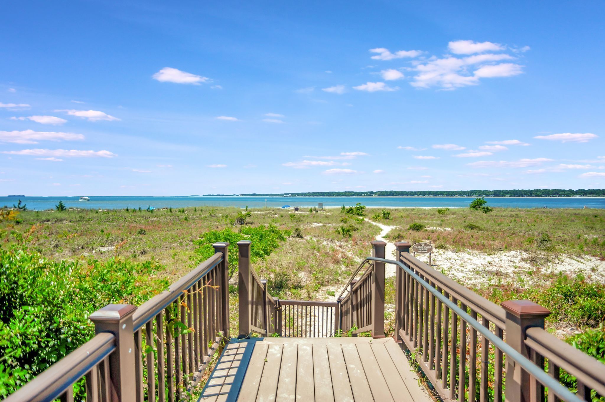 A wooden boardwalk leading to a beach with a clear view of the ocean and distant land.
