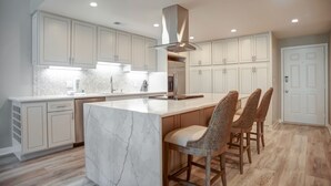 A modern kitchen with white cabinetry, a marble island, and bar stools.
