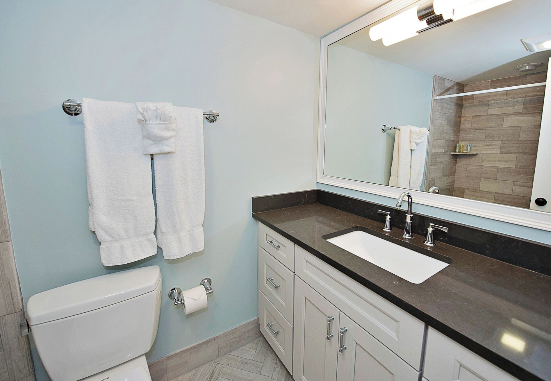 A bathroom with a toilet, sink, mirror, and towel rack.