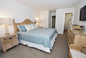 A bedroom with a bed, nightstands, a dresser, and a wicker chair. - 1255 Harbour Town Club at The Sea Pines Resort (Hilton Head Island)