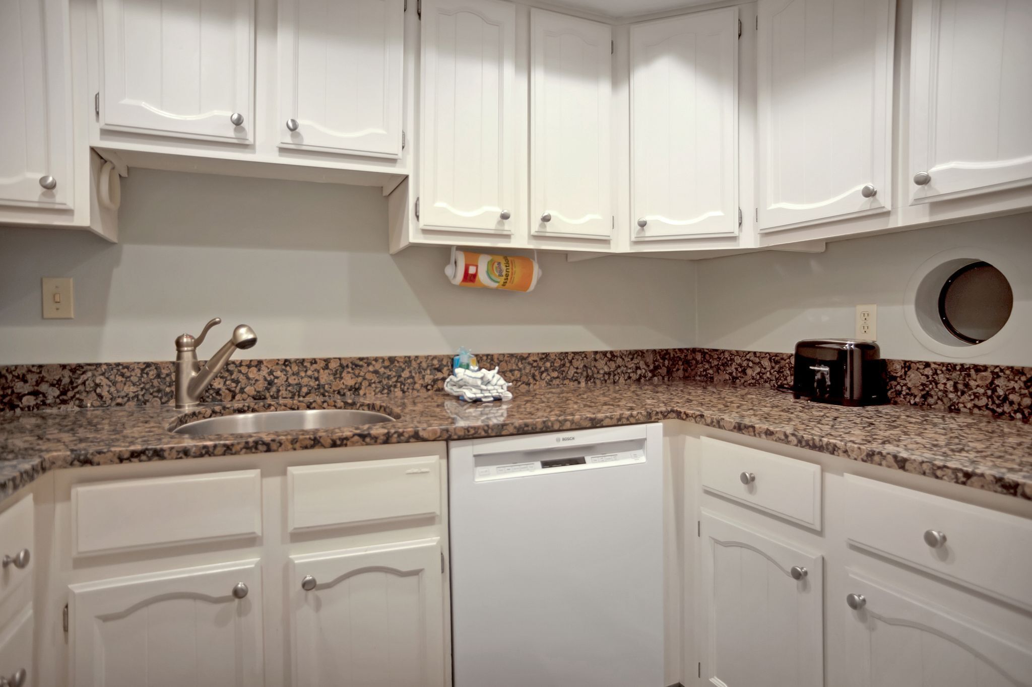 A kitchen with white cabinets, a granite countertop, a Bosch dishwasher, and a toaster.