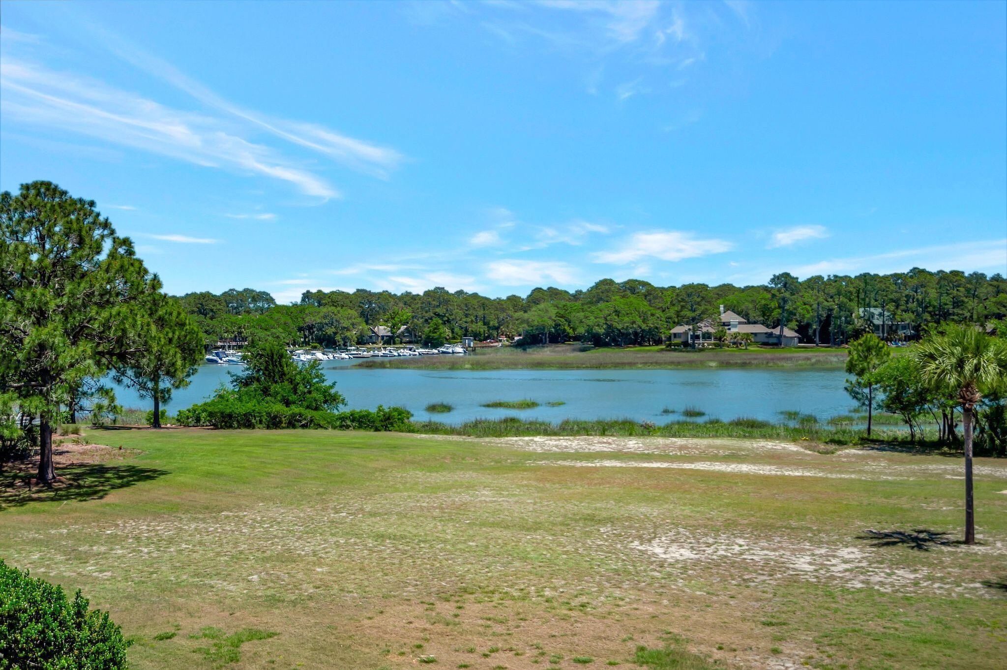 A lakeside view with a grassy area, trees, and a dock with boats.