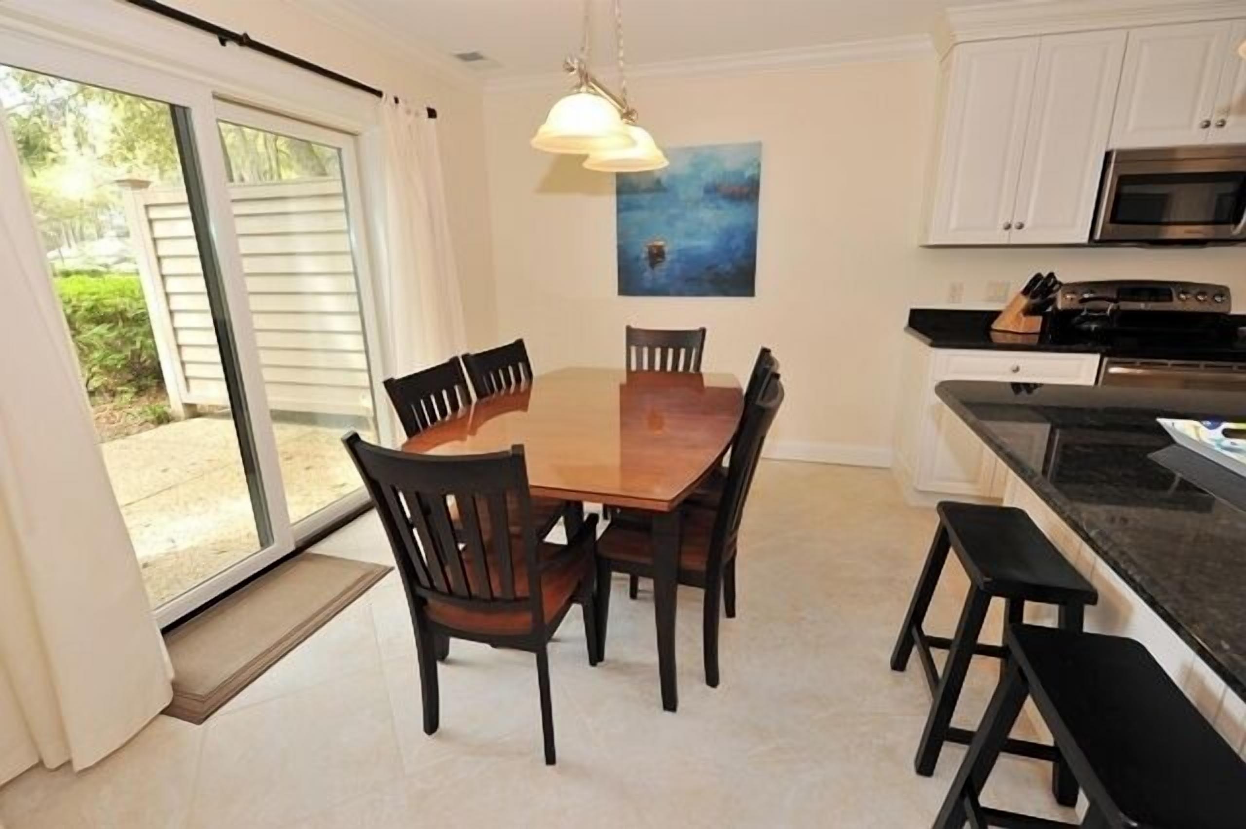 A dining area with a wooden table and chairs, a black countertop with a microwave, and a sliding glass door leading to an outdoor area.