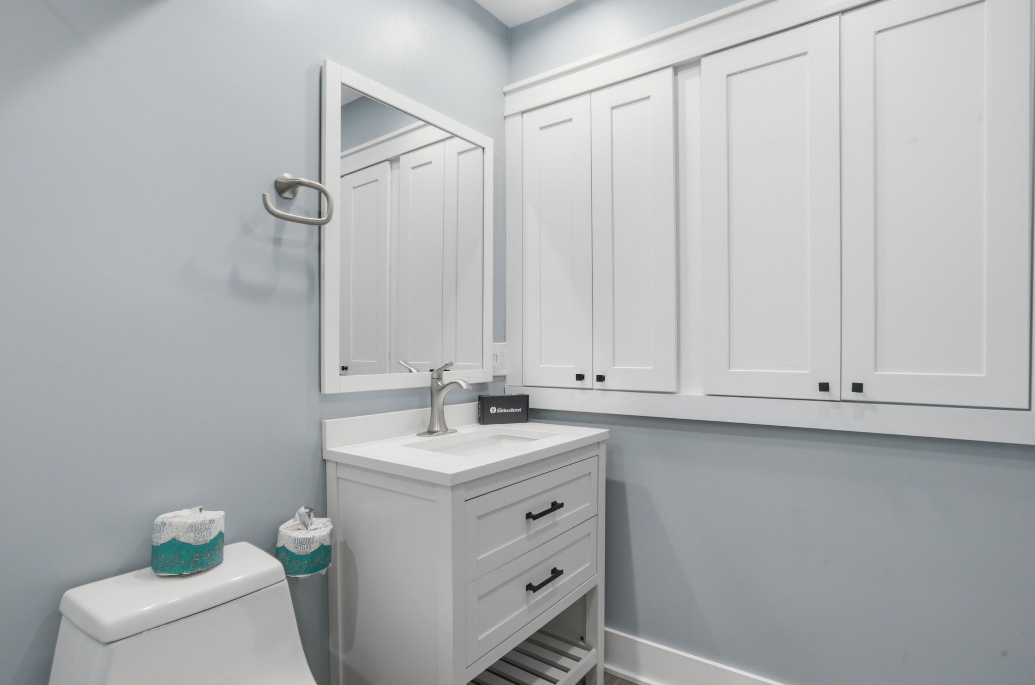 Une salle de bain avec un lavabo blanc, un miroir et des placards, ainsi qu’une toilette équipée de papier toilette.