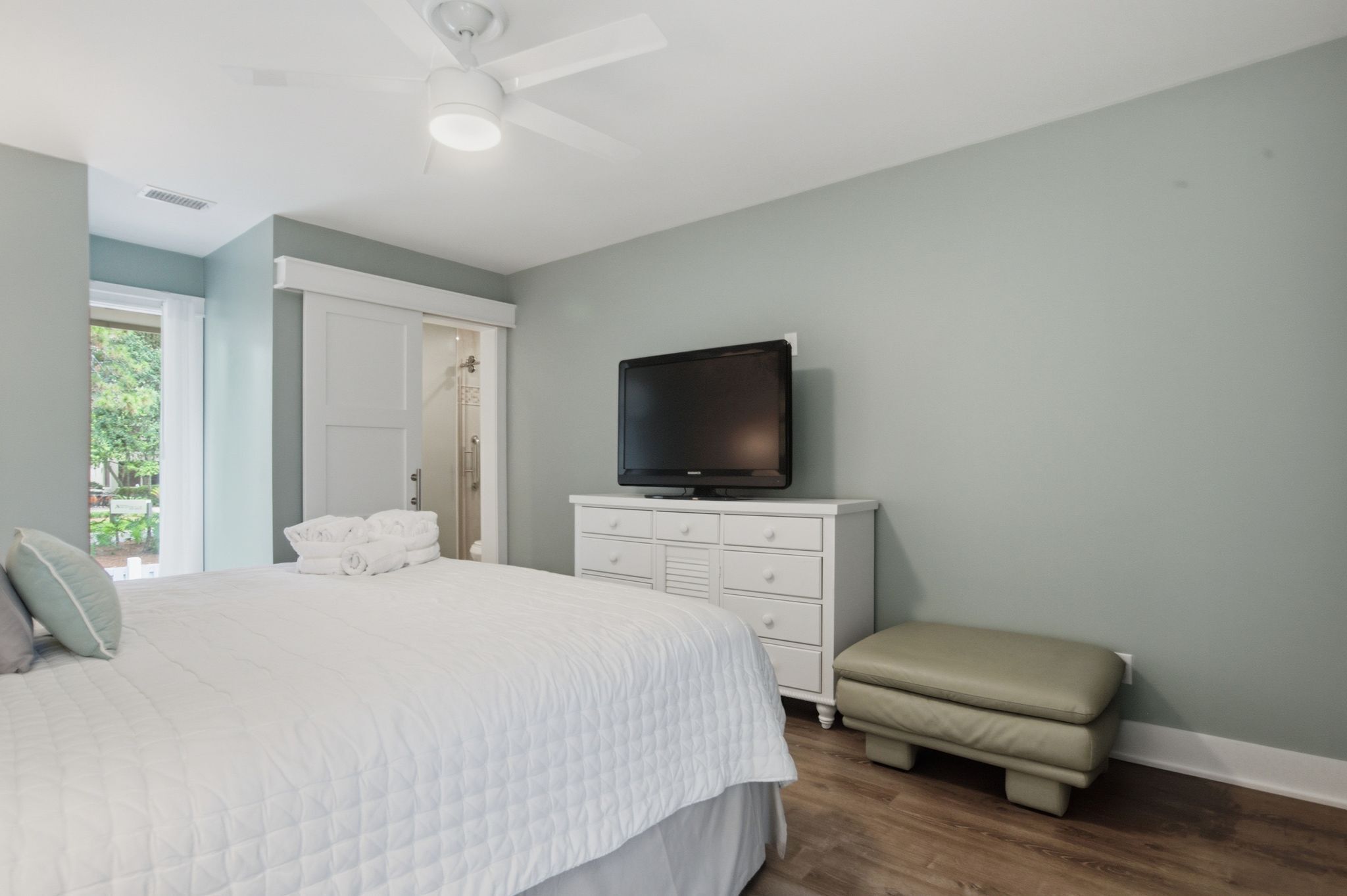Une chambre à coucher avec un lit, un téléviseur posé sur une commode, un banc et une porte donnant sur une salle de bain.