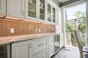 A kitchen with white cabinets, a brick backsplash, and a view of a residential area through a large window.