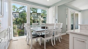 Une cuisine moderne avec des meubles blancs, un coin repas avec des chaises blanches et une vue sur un quartier résidentiel.