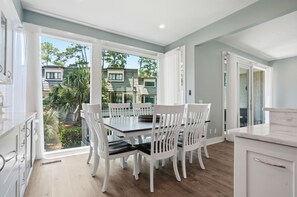 Une cuisine moderne avec des meubles blancs, un coin repas avec des chaises blanches et une vue sur un quartier résidentiel.