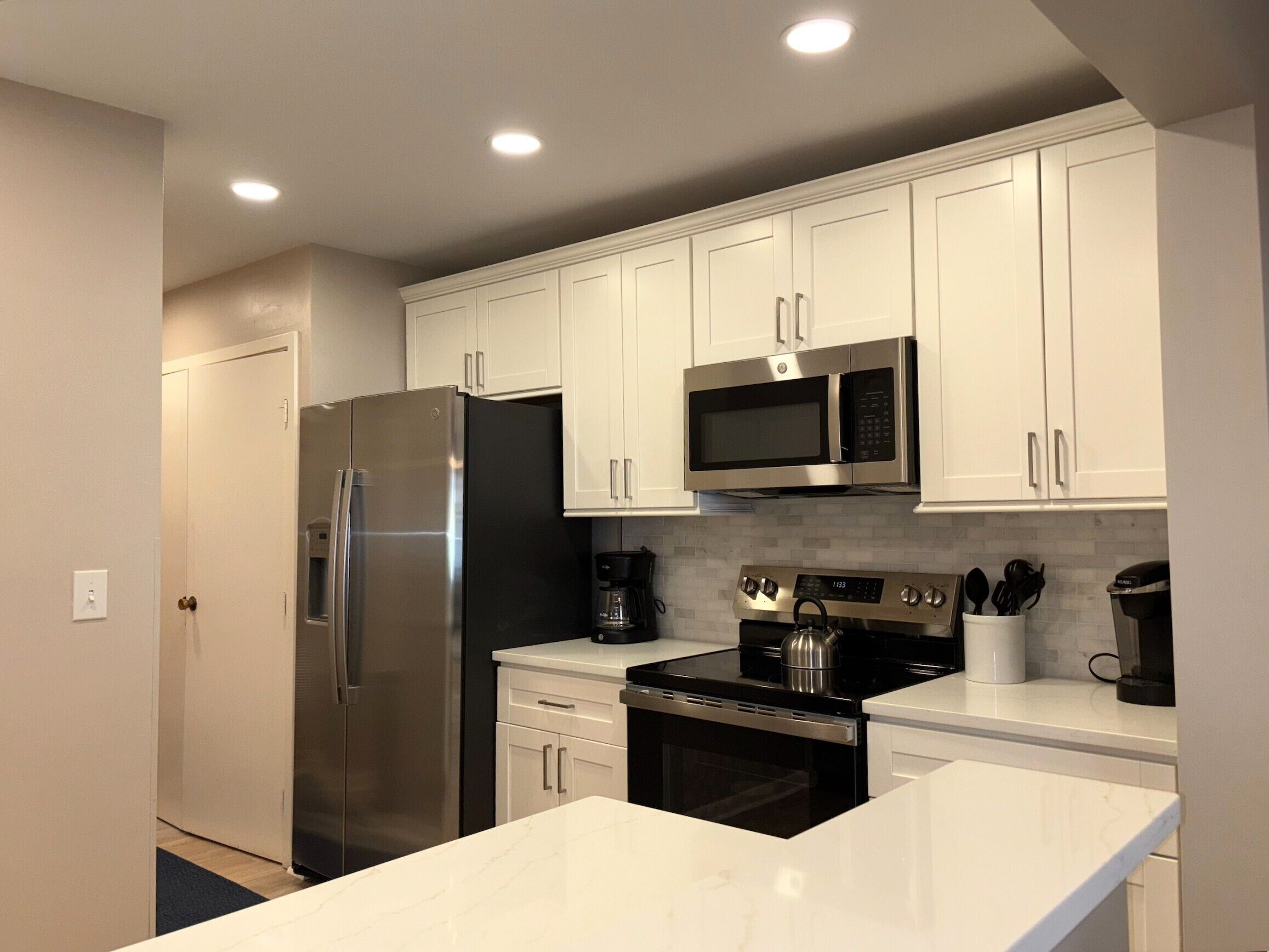 A modern kitchen with white cabinets, stainless steel appliances, and a marble countertop.