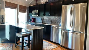 A modern kitchen with dark cabinets, a stainless steel refrigerator, a microwave, and a coffee maker. - 2070 Deer Island at The Sea Pines Resort (Hilton Head Island)