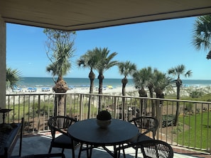 A covered patio with a view of the beach, featuring a round table and chairs, and a railing overlooking the ocean. - 2001 Turtle Lane at The Sea Pines Resort (Hilton Head Island)