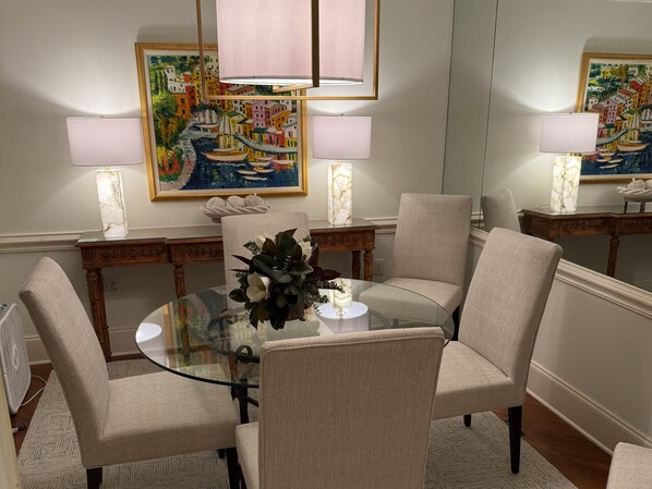 Un coin repas avec une table en verre entourée de quatre chaises, un centre de table floral et deux lampes de chaque côté.