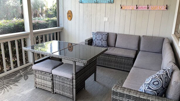 Un patio techado con una mesa de vidrio, muebles de mimbre y vistas al exterior con vegetación.