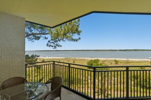 A balcony with a glass table and chairs, overlooking a beach and water. - 1892 Beachside Tennis at The Sea Pines Resort (Hilton Head Island)