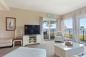Une chambre dâhĂŽtel Ă©quipĂ©e dâune tĂ©lĂ©vision, dâun canapĂ©, dâun fauteuil, dâune petite table et dâun balcon avec vue.